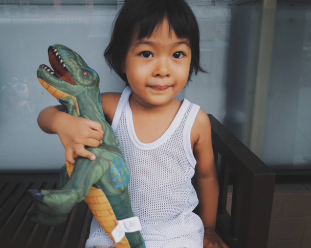 Niewyraźne zdjęcie stylu Vintage dziecko Asia dziewczyna uściski lalki dinozaurów szczęśliwie. Ona jest uśmiechnął się bardzo szczęśliwy, szczęśliwy pomysł dziewczyna dziecko, piękne zęby. - Zdjęcie, obraz