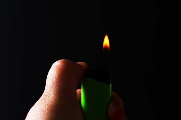Hand holding burning gas lighters on dark black background. Portable device used to create a flame - Photo, Image