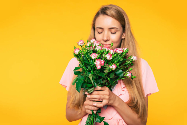 Beautiful smell. Portrait of lovely blonde woman while she is trying the smells of roses in her hands. Holidays and gifts concept. Women's day. St. Valentine's day - Photo, image