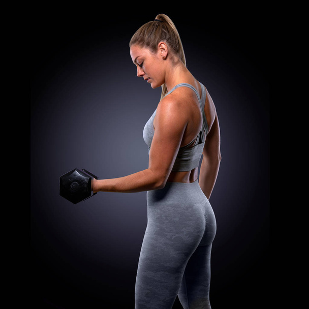 Ισχυρό μυϊκό ελκυστικό θηλυκό άσκηση με βάρη, τονισμένα χέρια, δικέφαλους, χρησιμοποιώντας βαράκια για την τόνωση του βραχίονα γυμναστικής και την ενίσχυση - Φωτογραφία, εικόνα