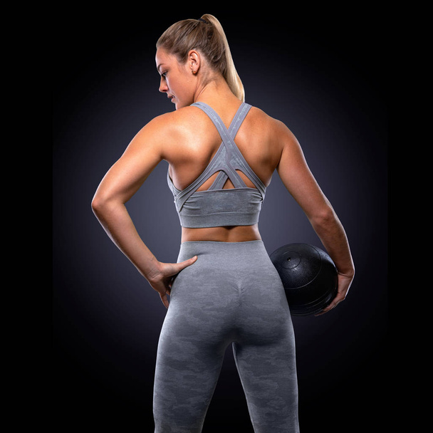 Forte posizione di forza fiduciosa, allenatrice donna con palla medica, glutei tonici, allenamento della parte superiore del corpo, posa maestosa da dietro, schiena, muscoli della schiena, culo, braccia
 - Foto, immagini