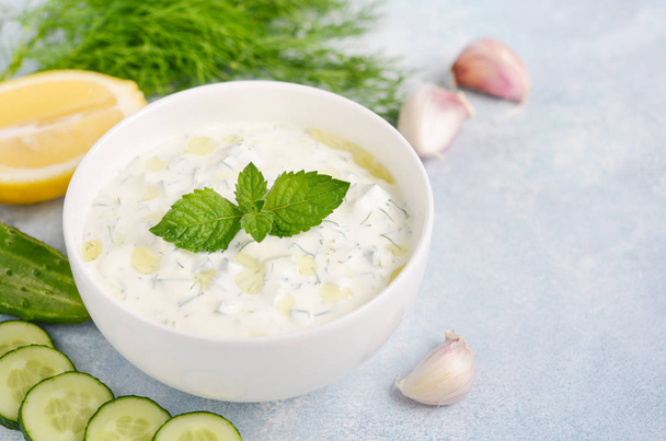 Greek dip sauce or dressing tzatziki decorated with olive oil and mint on blue background. - Foto, imagen