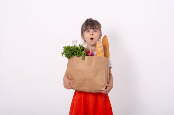 Cute little girl with food in grocery bag from grocery market in hands. With copy space for text, isolated. - Photo, Image