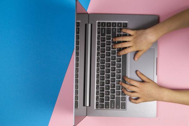Дитячі руки, що друкуються на клавіатурі комп'ютера ноутбука, вид зверху, рожевий і синій фон
 - Фото, зображення