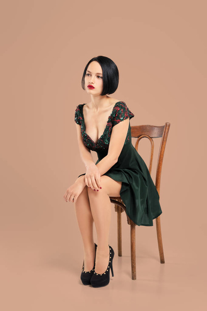 Gorgeous lady in short dress sitting on chair in studio with beige background - Foto, Imagen