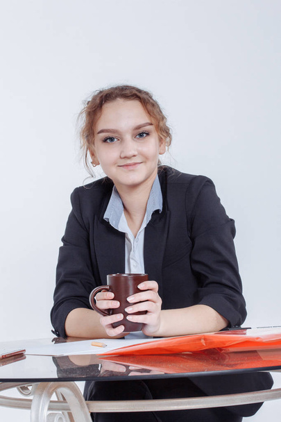 education, people, children and school concept - Portrait of young beautiful woman sitting at desk enjoying cup of coffee while working or studying at small home office or in the student dorm. Indoors - Фото, зображення
