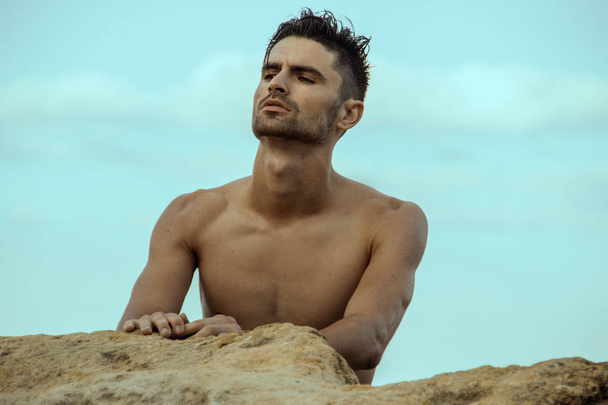 Strong face male model on the nature background with rocks sand and water on the beach on the sunset - Foto, imagen