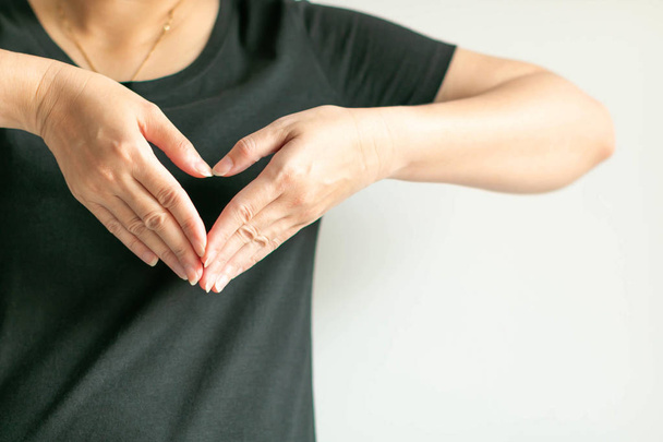 Kobieta używać rąk wyświetlić symbol miłości przez splice palców razem do kształtu serca na przedniej lewej klatki piersiowej. - Zdjęcie, obraz