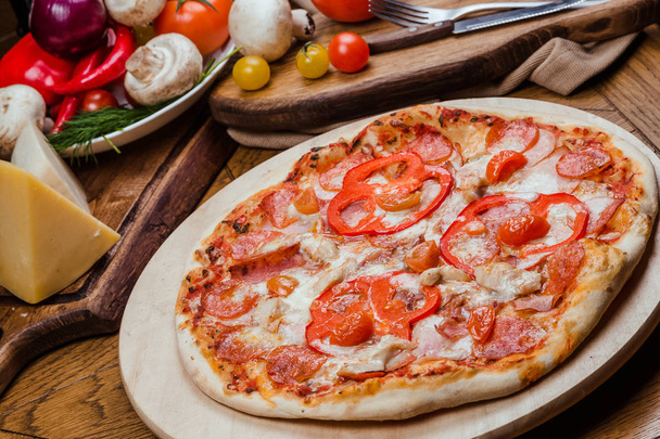 salami pizza on a wooden board, wooden background decorated with vegetables and cutlery - Photo, image