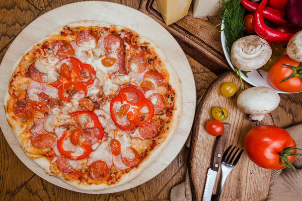 salami pizza on a wooden board, wooden background decorated with vegetables and cutlery - Foto, Imagem