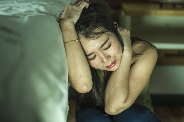 dramatic lifestyle portrait of young depressed and sad Asian Chinese woman sitting on floor at bedroom next to bed suffering depression problem and anxiety crisis - Fotografie, Obrázek