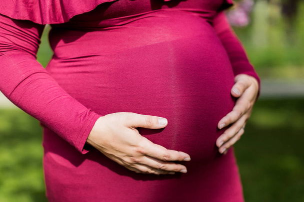 kobieta w ciąży trzymająca się za ręce w parku - Zdjęcie, obraz