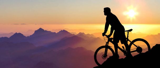 Fietser in shorts en Jersey op een moderne carbon hardtail fiets met een luchtgeveerde vork rijdt Off-Road op de oranje-rode heuvels bij zonsondergang avond in de zomer - Foto, afbeelding