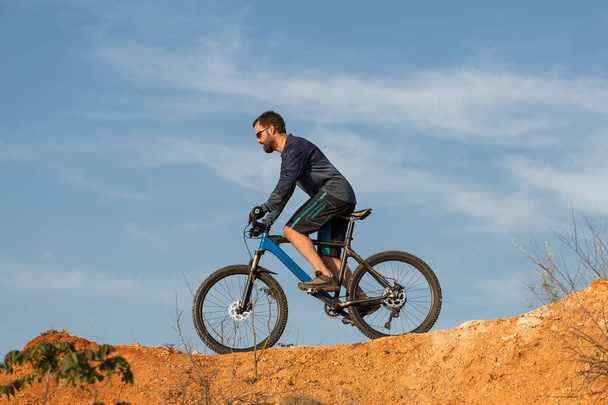 Cyklista v trenýrkách a v Jersey na moderním uhlíkově tvrdém kole se vzduchovou pružovou odbočku na oranžově červeném kopci při západu slunce v létě - Fotografie, Obrázek