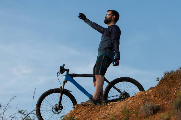 Cyclist in shorts and jersey on a modern carbon hardtail bike with an air suspension fork rides off-road on the orange-red hills at sunset evening in summer - Photo, Image