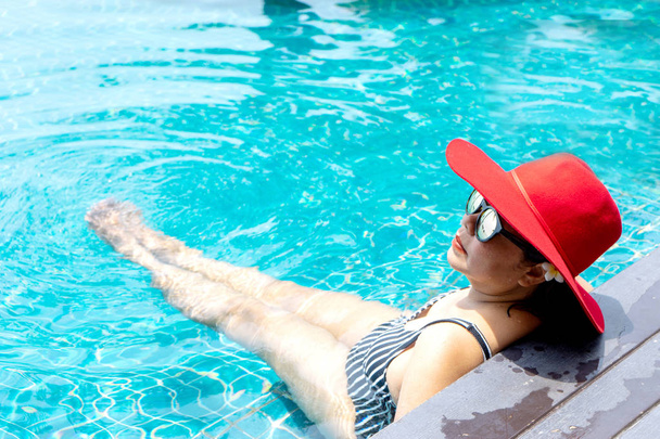 Азійка з червоним капелюхом відпочиває у басейні..  - Фото, зображення