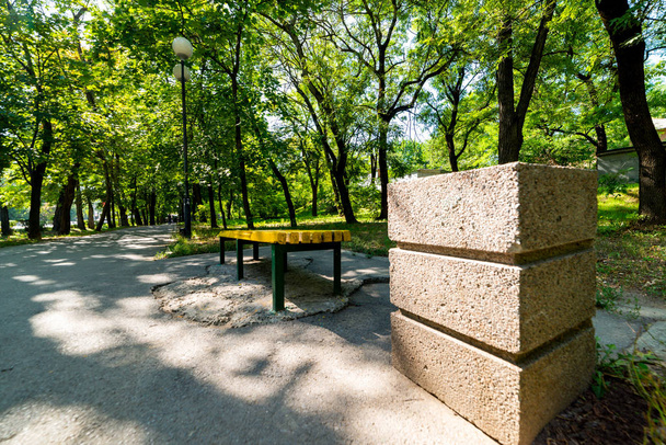 Un banc en bois jaune dans le parc en soirée d'été au soleil. A proximité se trouve une poubelle en béton carré
 - Photo, image
