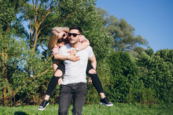 Girl sitting on the back of a man hugging and smiling in nature in summer - Foto, afbeelding