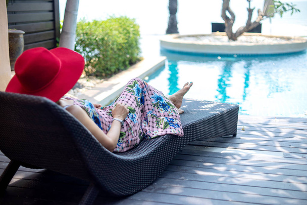 Καλοκαιρινό lifestyle γυναίκα με κόκκινο καπέλο ξαπλωμένη σε ξαπλώστρα κοντά στην πισίνα. - Φωτογραφία, εικόνα