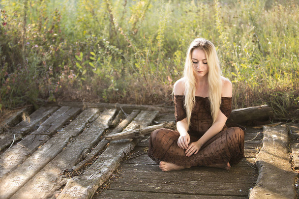 молода красива жінка сидить на старій дерев'яній підлозі в саду
 - Фото, зображення