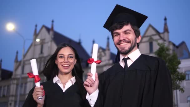 Diplomalarını gösteren iki mutlu mezun öğrenci kameraya poz veriyor. Rüzgar kızların kafalarını uçuruyor.. - Video, Çekim