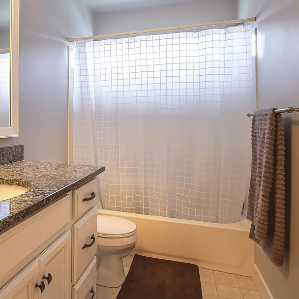 Interior do banheiro quadrado com banheiro ao lado de uma unidade de vaidade com grande espelho retangular
 - Foto, Imagem