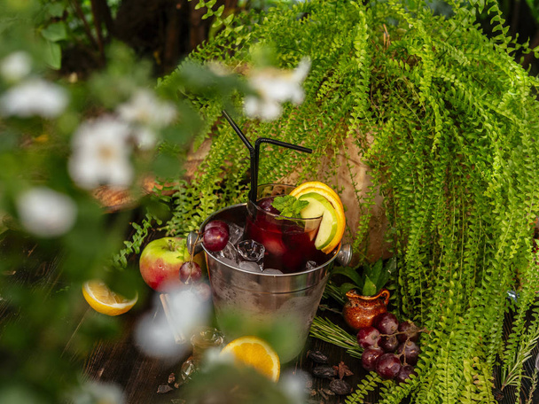 Red alcoholic cocktail in a bucket with ice. Garnished with fruits and berries on a wooden table. - Foto, Imagen