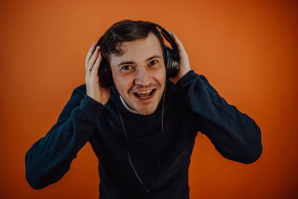 A beautiful young man in headphones with ears is dancing on an orange background. The concept of International Music Day. - Valokuva, kuva