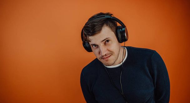 A beautiful young man in headphones with ears is dancing on an orange background. The concept of International Music Day. - Фото, изображение