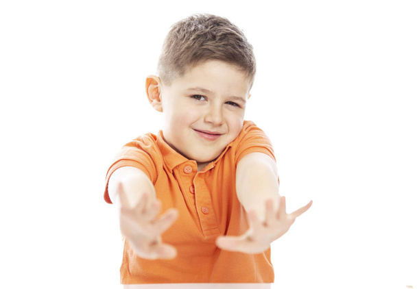 A smiling school-age boy in a bright orange polo t-shirt sits at a table, arms extended forward. Close-up. Isolirvoan on a white background. - Foto, Bild