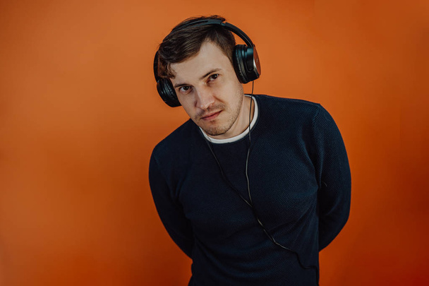 A beautiful young man in headphones with ears is dancing on an orange background. The concept of International Music Day. - Fotografie, Obrázek