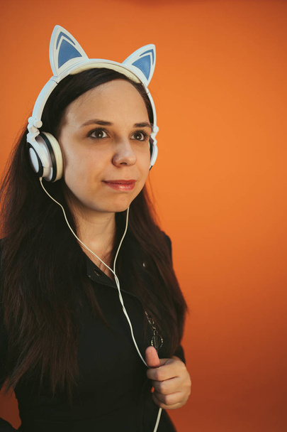 A beautiful young woman in headphones with ears is dancing on an orange background. The concept of International Music Day. - Photo, Image