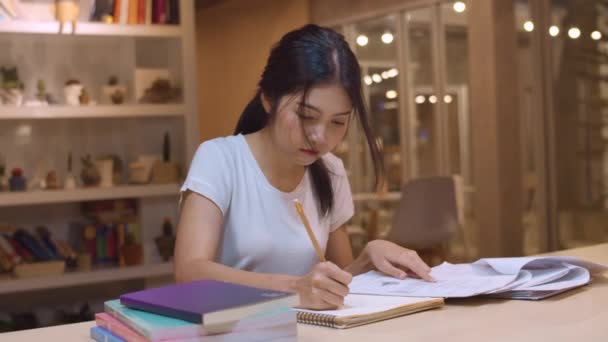 大学の図書館で本を読むアジアの学生の女性。若い学部生の女の子は宿題をし、教科書を読み、大学のキャンパスの残業時間の夜に講義デスクで知識のために一生懸命勉強します。スローモーション. - 映像、動画