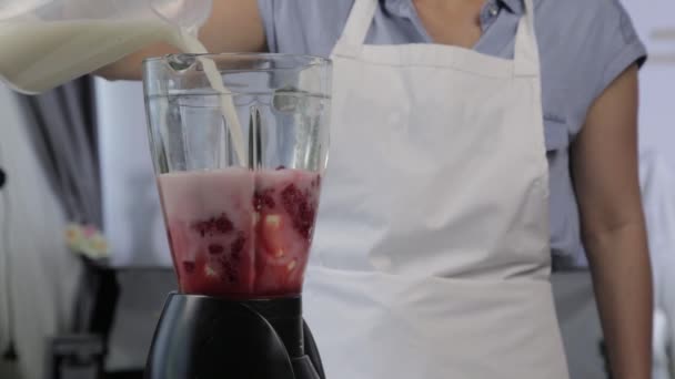 young woman cooking a fruit and berry cocktail in a blender. Pouring milk in blender with raspberries. healthy eating and dieting concept - Footage, Video