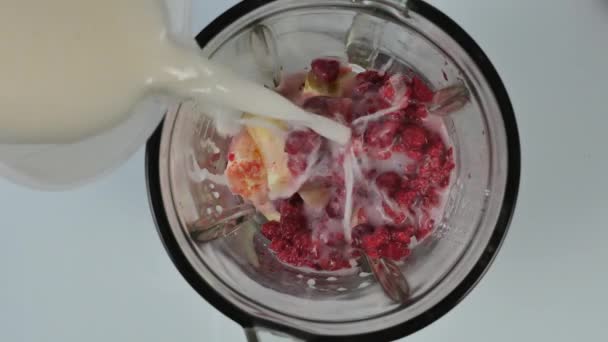 young woman cooking a fruit and berry cocktail in a blender. Pouring milk in blender with raspberries. healthy eating and dieting concept - Filmmaterial, Video