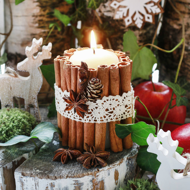 Candle decorated with cinnamon sticks, moss, ivy leaves and wood - Фото, изображение