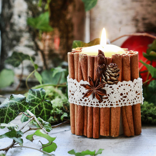 Candle decorated with cinnamon sticks, moss, ivy leaves and wood - Foto, afbeelding