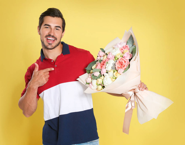 Young handsome man with beautiful flower bouquet on yellow background - Photo, Image