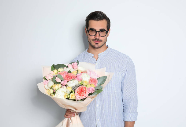 Hafif arka planda güzel çiçek buketi ile genç yakışıklı adam - Fotoğraf, Görsel