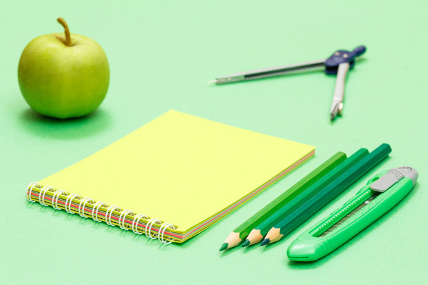 School benodigdheden. Apple, kompas, notebook, kleurpotloden en papier mes op de groene achtergrond. - Foto, afbeelding