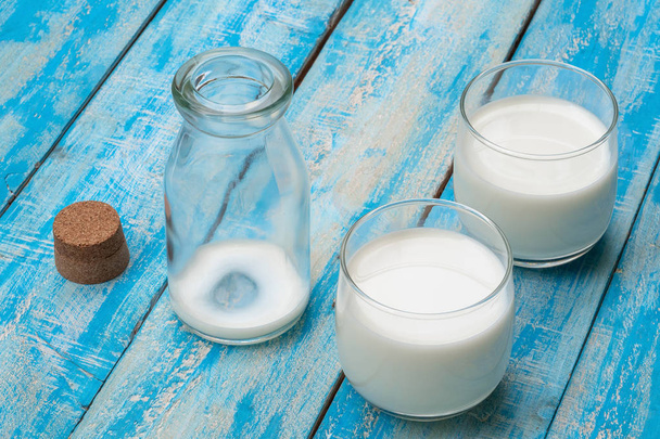 Una bottiglia di latte e un bicchiere di latte su un tavolo di legno blu, guarire
 - Foto, immagini