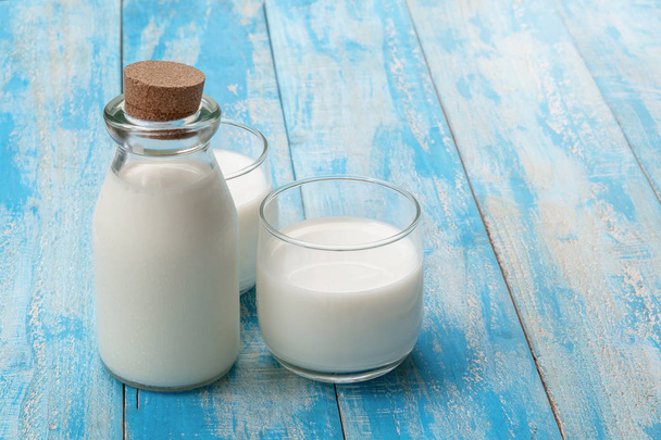 Láhev mléka a sklenice mléka na modrém dřevěném stole, léčený - Fotografie, Obrázek