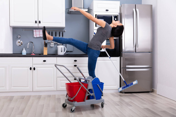 Close-up Of A Young Woman Slipping While Mopping Floor In The Kitchen - 写真・画像