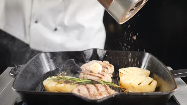 Close-up shot van chef-kok koken aardappel en vlees op grill. Professionele kookplaat voegt peper toe in slow motion. Hd - Video