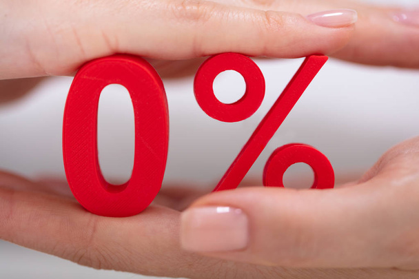 Businessperson's Hand Protecting Red Zero Percentage Icon Over White Desk - 写真・画像