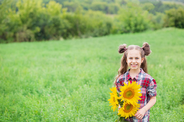 Portrét malé dívky s velkou nádhernou slunečnicovou kyticí v dlaních na pozadí polí. - Fotografie, Obrázek