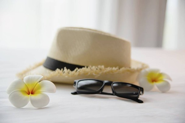 Tourist stuff hat sun glasses and plumeria flower in white bed room - happy relax vacation holiday and hotel concept - 写真・画像