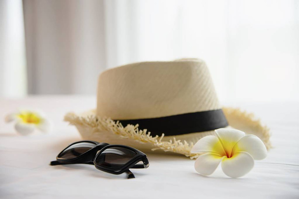 Tourist stuff hat sun glasses and plumeria flower in white bed room - happy relax vacation holiday and hotel concept - Foto, afbeelding