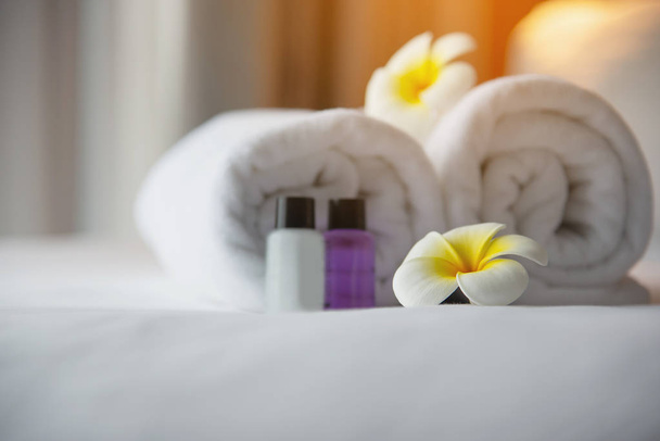 Hotel towel and shampoo and soap bath bottle set on white bed with plumeria flower decorated - relax vacation at the hotel resort concept - Photo, Image