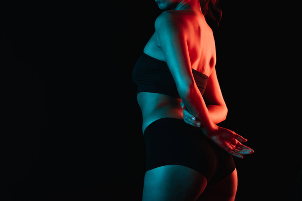 обрізаний вид освітлення на молоду жінку в нижній білизні, що стоїть ізольовано на чорному
  - Фото, зображення